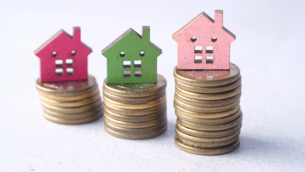 Small cardboard homes on top of stacked piles of coins