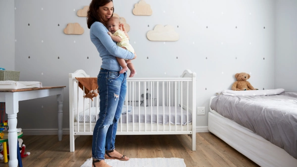 A mother holding a baby to her chest in a decorated nursery.