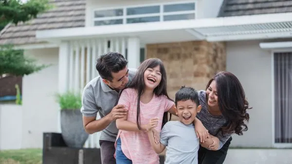 Couple laughing with kids in front yard of home