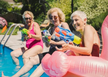 Three women play with water guns at a pool