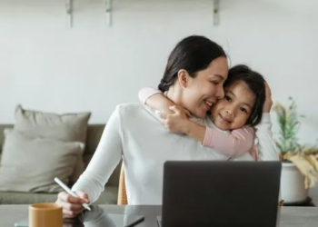 Mom working on laptop child hugging her