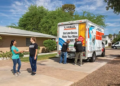 A customer shakes hands with a Moving Help Service Provider after completing a successful job of loading the customer’s belongings into a U-Haul truck rental. Two labor-only providers in the background close the U-Haul truck rental.