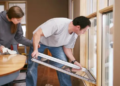 Two people sealing gaps and cracks around a window.