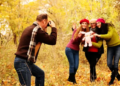 A family taking photos with fall leaves in the back.