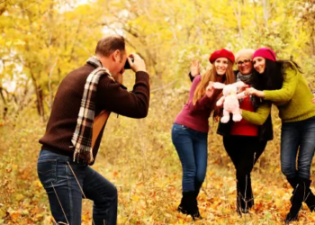 A family taking photos with fall leaves in the back.