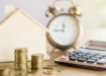 Coins, calculator, a clock and a small, wooden house.