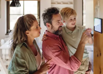 Two people holding a kid, looking at a thermostat in a sustainable home.