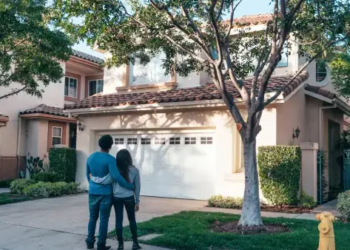 Two people stand outside of a home looking at it from the outside.